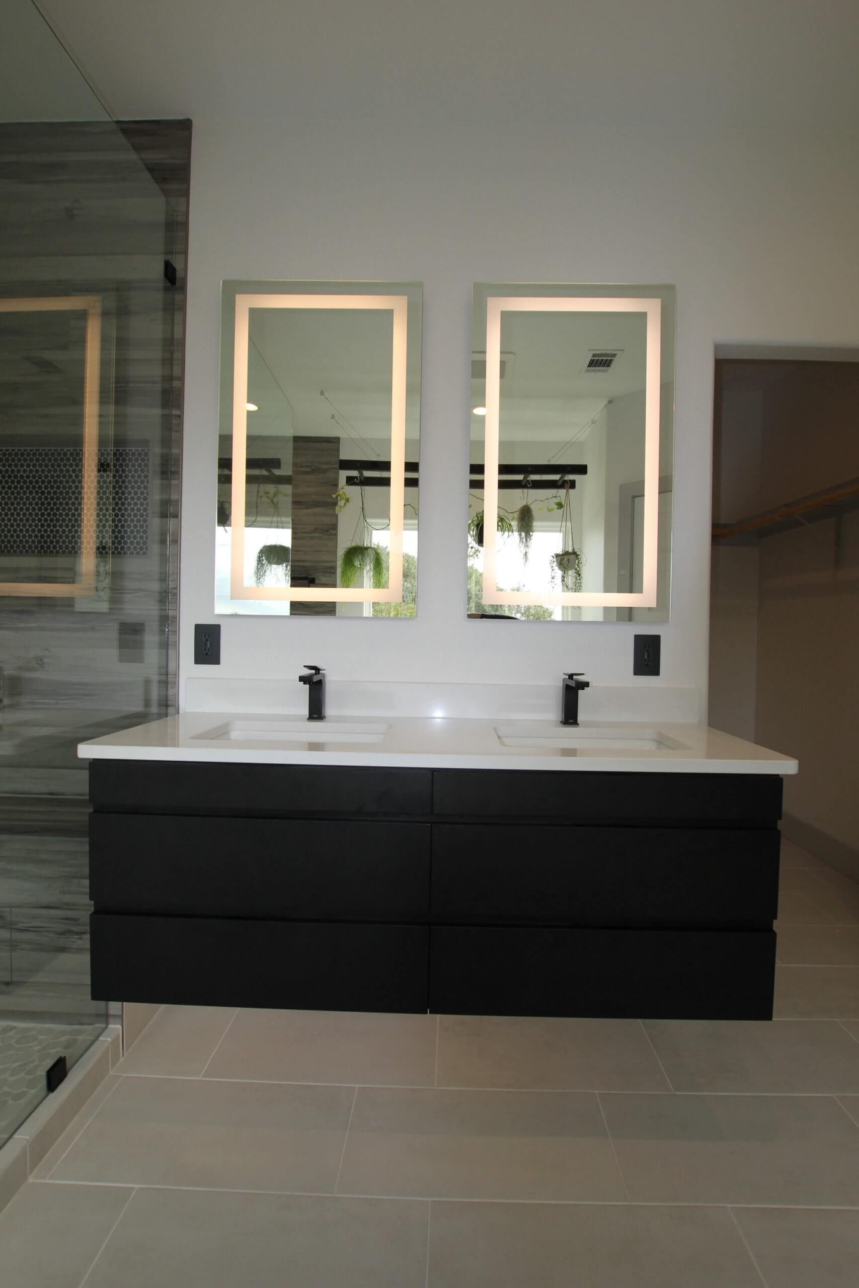 Floating black bathroom cabinets with double sinks and two LED lit vanity mirrors