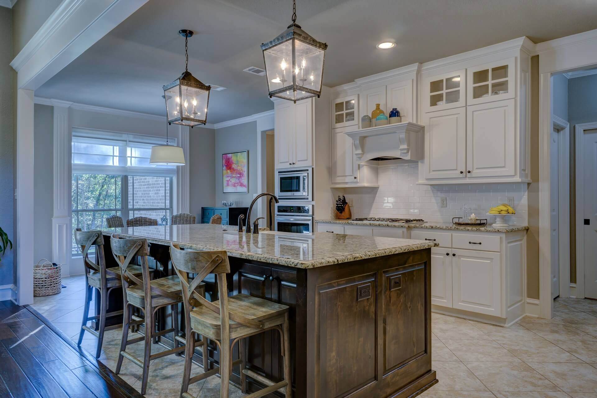 A southern styled kitchen with white cabinets, tan tiled floors, and an island bar in the middle