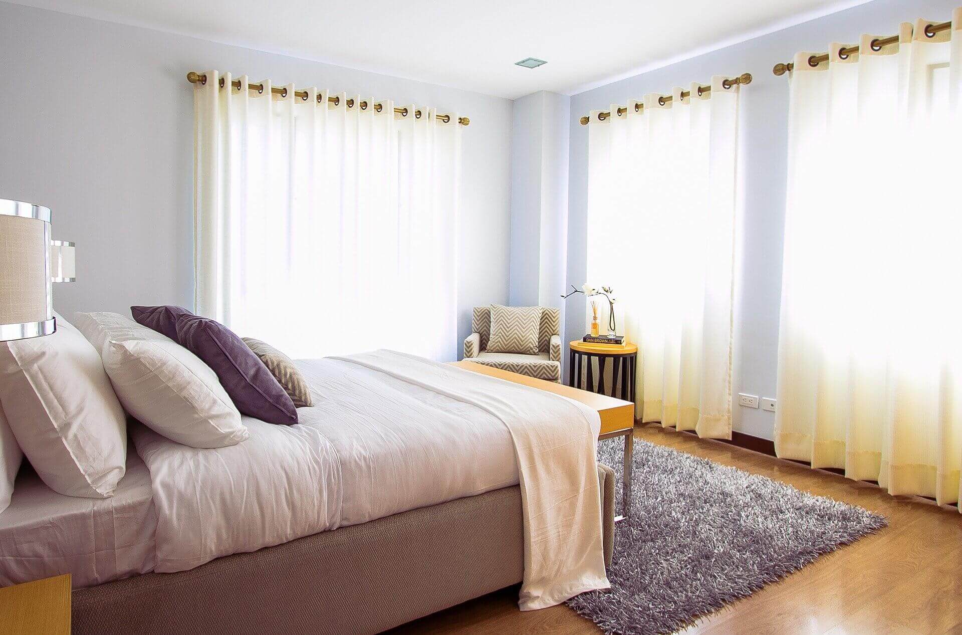 Modern master bedroom with a purple shag rug and large windows with tan curtains