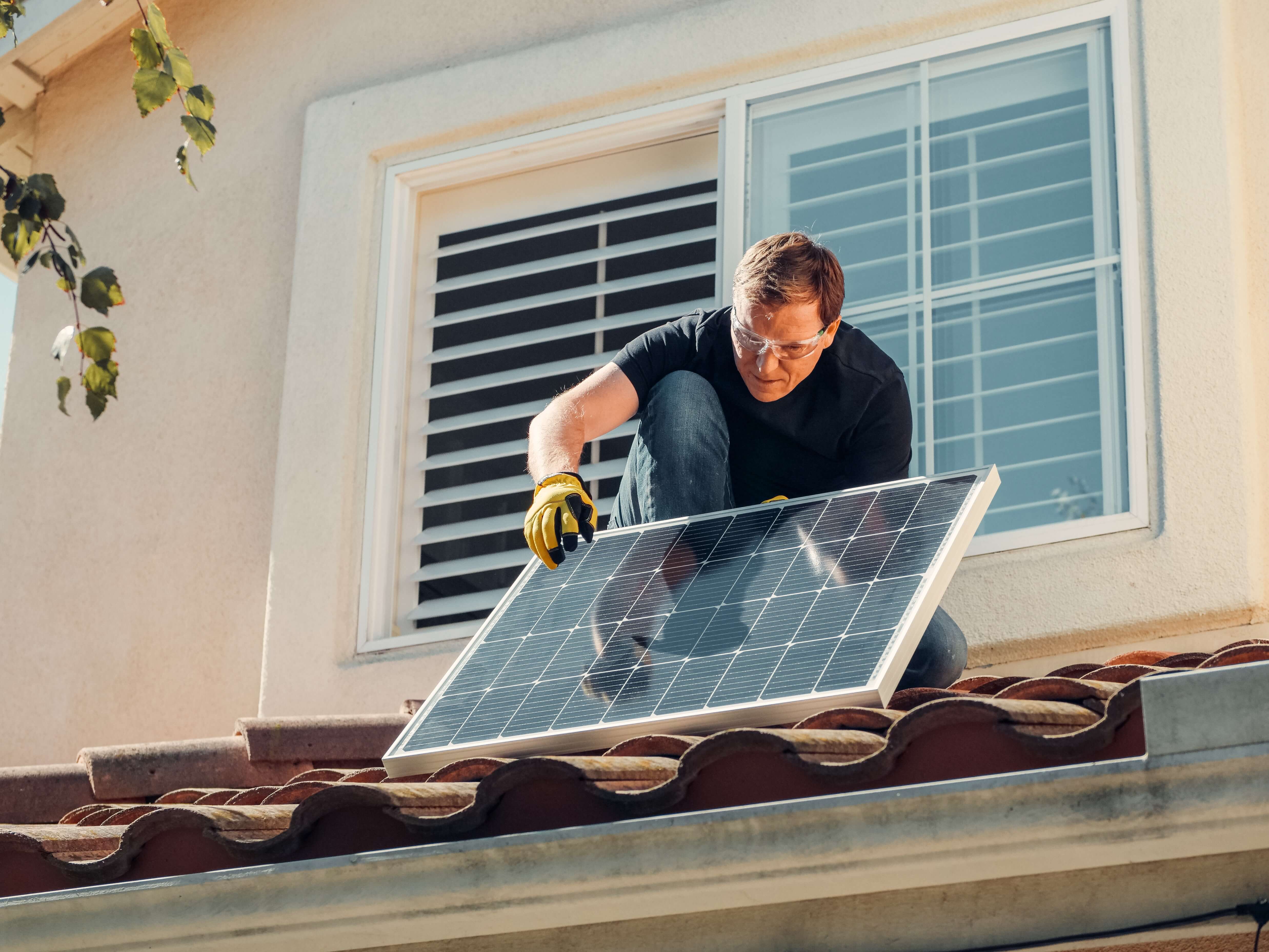 A man installing solar panels to make a house more sustainable.